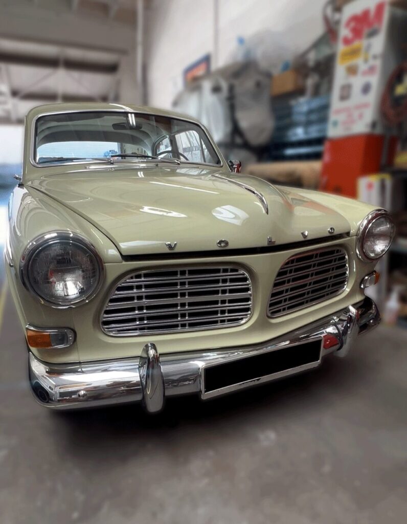 Front view of a vintage beige-green Volvo Amazon parked in a garage
